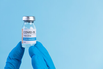 Hand in protective glove holds Covid-19 Vaccine glass vial.