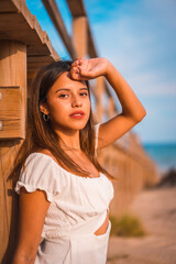 Lifestyle of a young Caucasian brunette enjoying the beach vacation in a white dress in summer, next to a wooden walkway