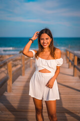 Lifestyle of a young brunette Caucasian on vacation on the beach wearing a white dress in summer, walking along the wooden walkway