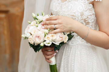 Hands of a young girl with a beautiful manicure and rings hold of fresh white roses. The bride in a white dress holds a classic wedding bouquet