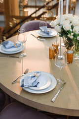a wooden table set with white plates and blue napkins. Fresh flowers on the table on the background of the dome from the windows