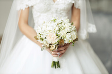 Hands of a young girl with a beautiful manicure and rings hold of fresh white roses. The bride in a white dress holds a classic wedding bouquet