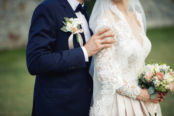 The bride and groom are standing next to each other and a man in a blue stylish suit with a bow-tie gently holds her by the shoulders