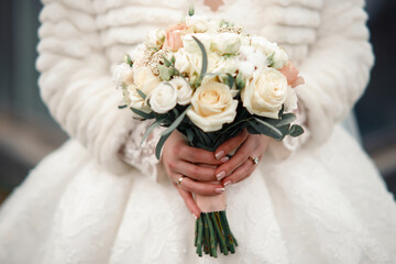 Hands of a young girl with a beautiful manicure and rings hold of fresh white roses. The bride in a...