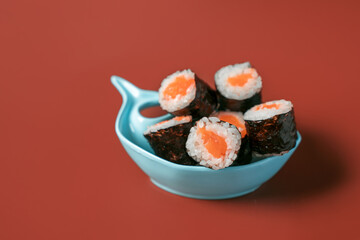Simple rolls with rice and salmon in a fish-shaped bowl on a burgundy background