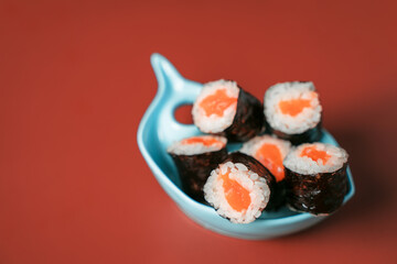 Simple rolls with rice and salmon in a fish-shaped bowl on a burgundy background