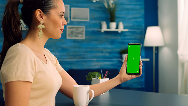 Freelancer using mock up green screen chroma key mobile during online videocall talking with her teamates about online app project standing on office desk. Business woman using isolated technology
