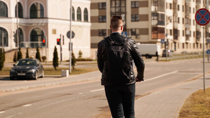 Back of a man with a black backpack. A man rides an electric scooter