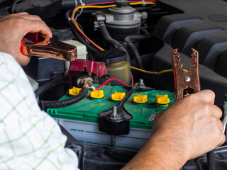 Man's hand holding the battery extension cable with brass clamps. Red insulated plastic cladding