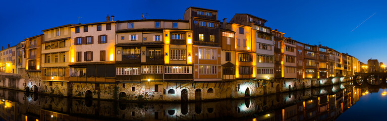 Scenic panoramic view of illuminated houses along Agout river in French city of Castres in twilight