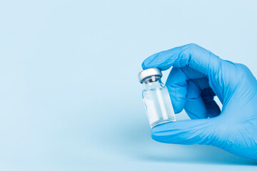 Hand in protective glove holds vaccine glass vial.