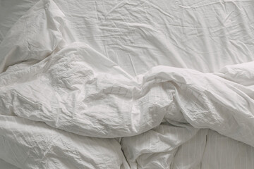 Rumpled white bed sheet and blanket on bed in the morning.