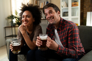 Boyfriend and girlfriend drinking beer at home. Happy couple watching sports game on tv..