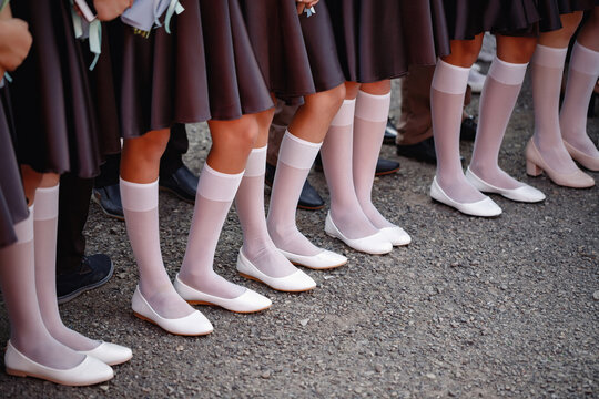 Teenage Girls With Tanned Legs In Dark Short Skirts, Long White Golfs And White Ballet Shoes, Pumps, Shoes Stand In A Line On The Street Without Faces. Ruler At School, Girls In School Uniform