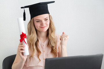 Woman student in masters hat with diploma behind a laptop. Online education, graduation concept