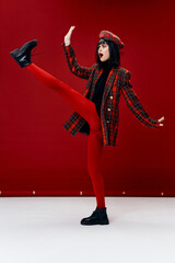 brunette in a plaid coat in red leggings and a hat lifted her leg up