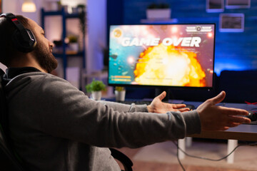 Naklejka premium Game over for gamer playing videogames on computer during night time in gaming room home. Defeated man with headphones streaming online cyber performing through tournament
