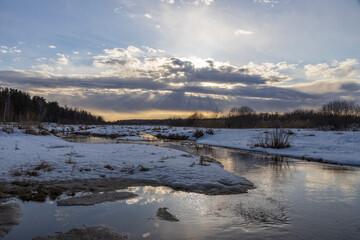 Sun through the clouds. Snow is melting. Early spring. Radiation of the river. Sun rays. Spring landscape