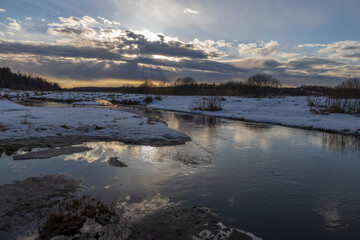 Sun through the clouds. Snow is melting. Early spring. Radiation of the river. Sun rays. Spring landscape