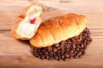 Croissant with coffe beans on wooden background