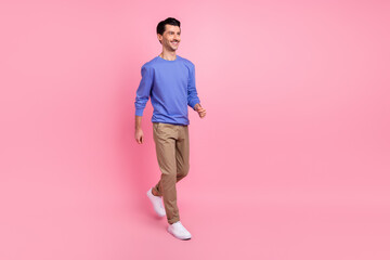 Full length photo of happy charming young guy look walk empty space good mood isolated on pink color background