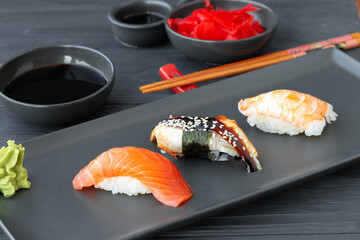 Nigiri sushi with salmon, eel and prawn served on black ceramic plate