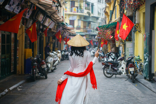 Vietnamese girl with traditional dress (ao dai) on Hanoi street with peach flower in hand during Tet holiday in Hanoi, Vietnam