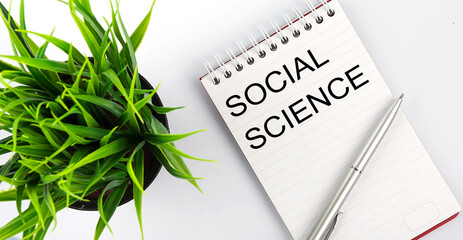 Keyword Social science - business concept text on a white notebook and pen, green flowers