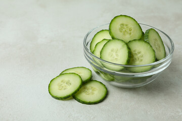 Bowl with cucumber slices on white textured background
