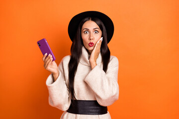 Portrait of attractive amazed woman using device browsing comment pout lips isolated over bright orange color background