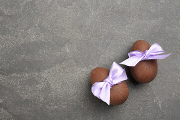 Sweet chocolate eggs with violet bows on grey table, flat lay. Space for text