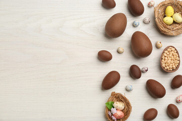Fototapeta na wymiar Sweet chocolate eggs and candies on white wooden table, flat lay. Space for text
