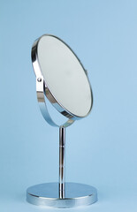 Mirror. Silver mirror. Blue background. Make-up mirror.Face care at home rotary mirror with...