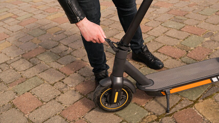 Young man folding an electric scooter in street outdoor.