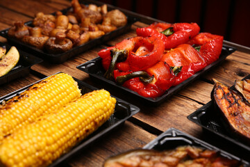 Plastic containers with different grilled meal on wooden table, closeup. Food delivery service