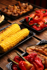 Plastic containers with different grilled meal on wooden table, closeup. Food delivery service