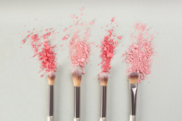 Makeup brushes and scattered eye shadows on light grey background, flat lay