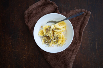 A close up of cereal bowl with sliced bananas sprinkled with chia seeds in a bowl on a dark background.
