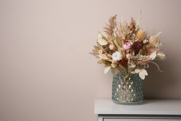 Beautiful dried flower bouquet in glass vase on white table near light grey wall. Space for text