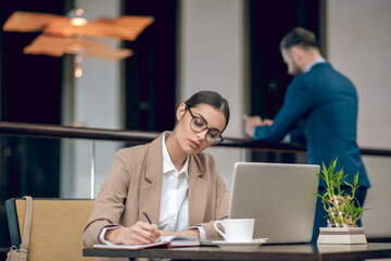 Young businesswoman in beige jacket working in the office and looking busy