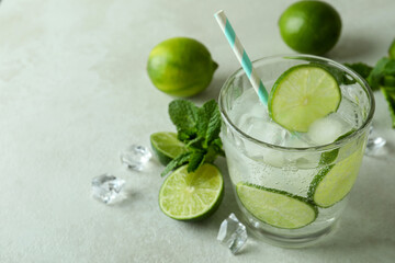Glass of mojito cocktail and ingredients on white textured background