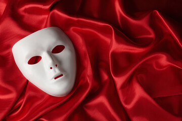 White theatre mask on red fabric, top view. Space for text