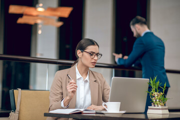 Young businesswoman in beige jacket working in the office and looking confident