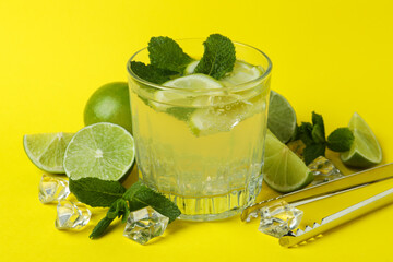 Glass of mojito cocktail and ingredients on yellow background
