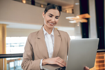 Young businesswoman in beige jacket standing with a laptop