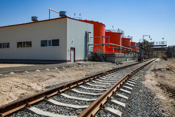 Fototapeta na wymiar Orange steel storage tanks with acid at (sulphuric) acid plant warehouse. Cargo railway terminal. Filling station. On the blue sky background