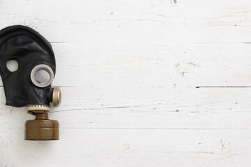 Old vintage gas mask in black on a white wooden background. Side view of a rubber gas mask with a filter.