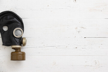 Old vintage gas mask in black on a white wooden background. Side view of a rubber gas mask with a...