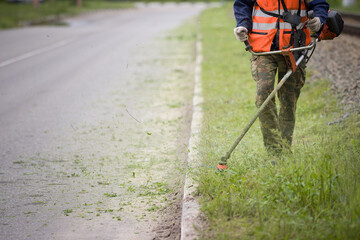 A worker in special reflective clothing with a gasoline mower in his hand. A man with a trimmer...