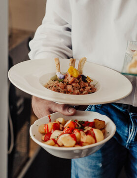Camarero llevando un tartar de salmon gourmet y una racion de patatas picantes en un restaurante de lujo